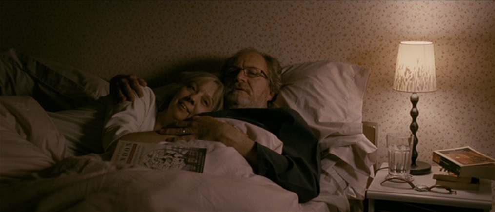 Film still from Another Year (2010) showing older couple cuddling in bed